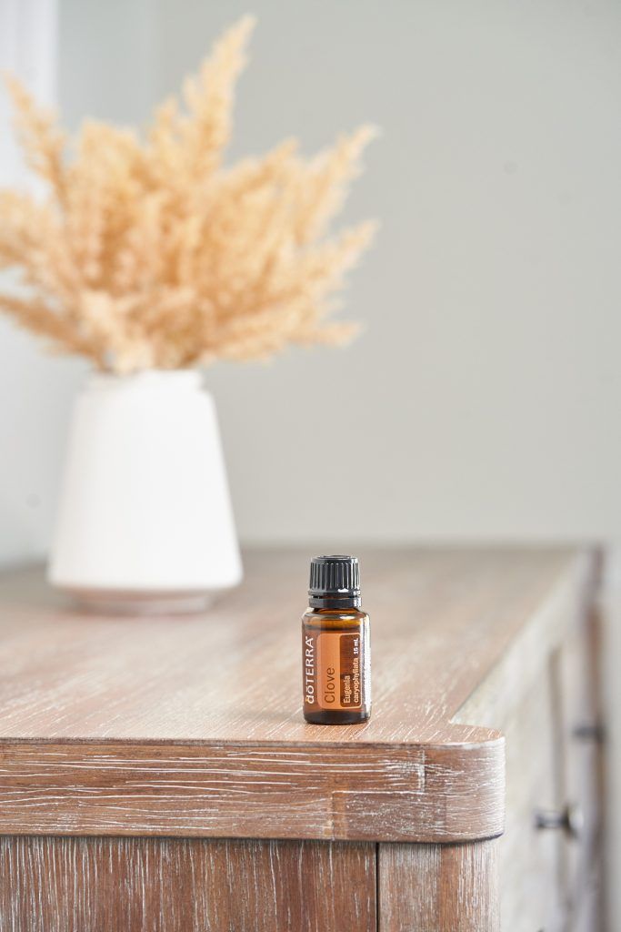 A doTERRA Clove essential-oil bottle on a wooden counter beside a vase of dried botanicals at Butterfly Massage Spa